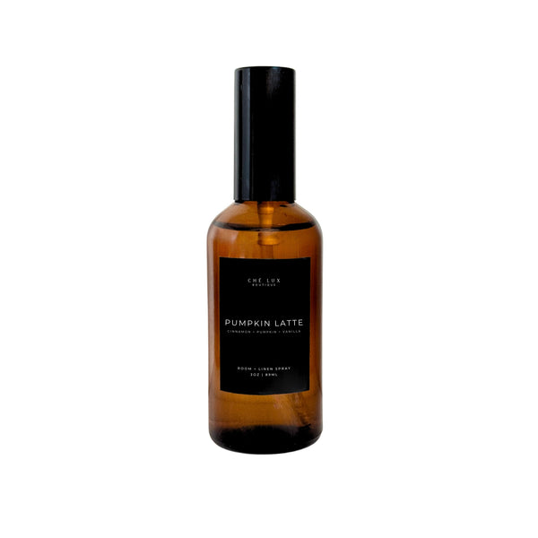Ché Lux Boutique amber glass room and linen spray bottle with a black label featuring PUMPKIN LATTE and CINNAMON + PUMPKIN + VANILLA scent notes, topped with a black spray nozzle