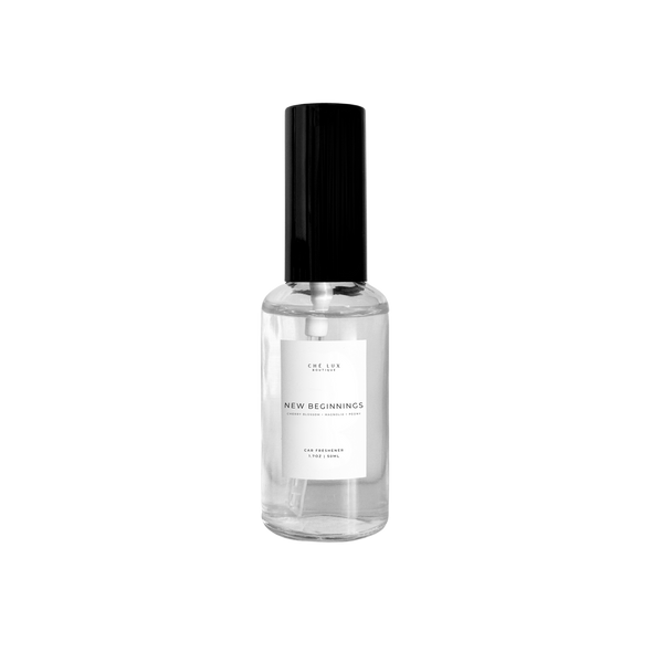Ché Lux Boutique car freshener a clear glass spray bottle with a black cap and white label displaying NEW BEGINNINGS scent cherry blossom magnolia and peony on a black background
