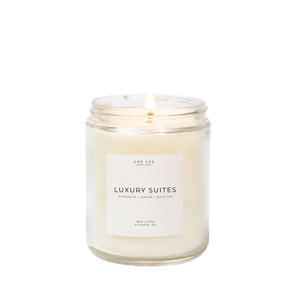 Product photograph of a Ché Lux Boutique Luxury Suites scented candle in a clear glass jar with white wax and a lit wick from Atlanta GA featuring a minimalist label with mandarin jasmine and white tea fragrance notes
