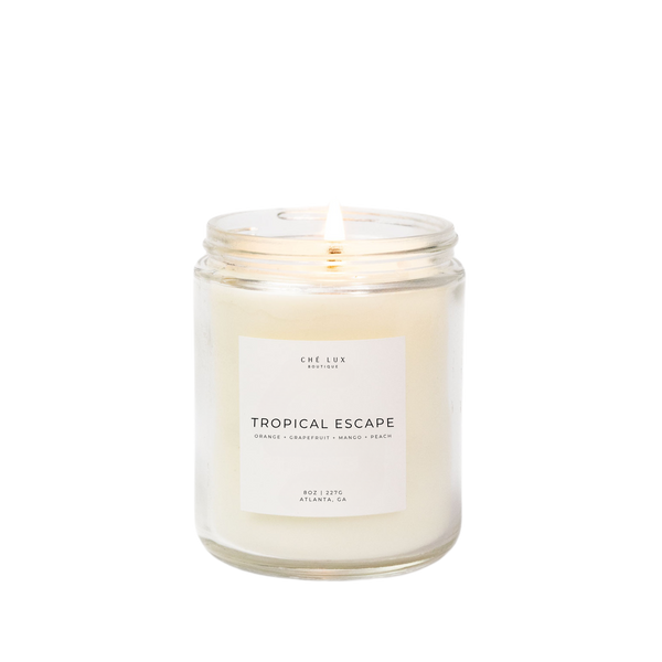 Product photo by Ché Lux Boutique of a lit 8oz Tropical Escape candle with creamy white wax in a clear glass jar from Atlanta GA, scented with orange grapefruit mango and peach