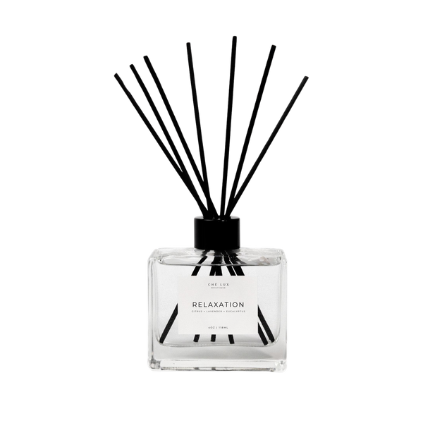 Product photo of a CHÉ LUX BOUTIQUE Relaxation reed diffuser in a clear rectangular glass bottle with black reeds and cap on a plain black background, highlighting citrus lavender eucalyptus scent details