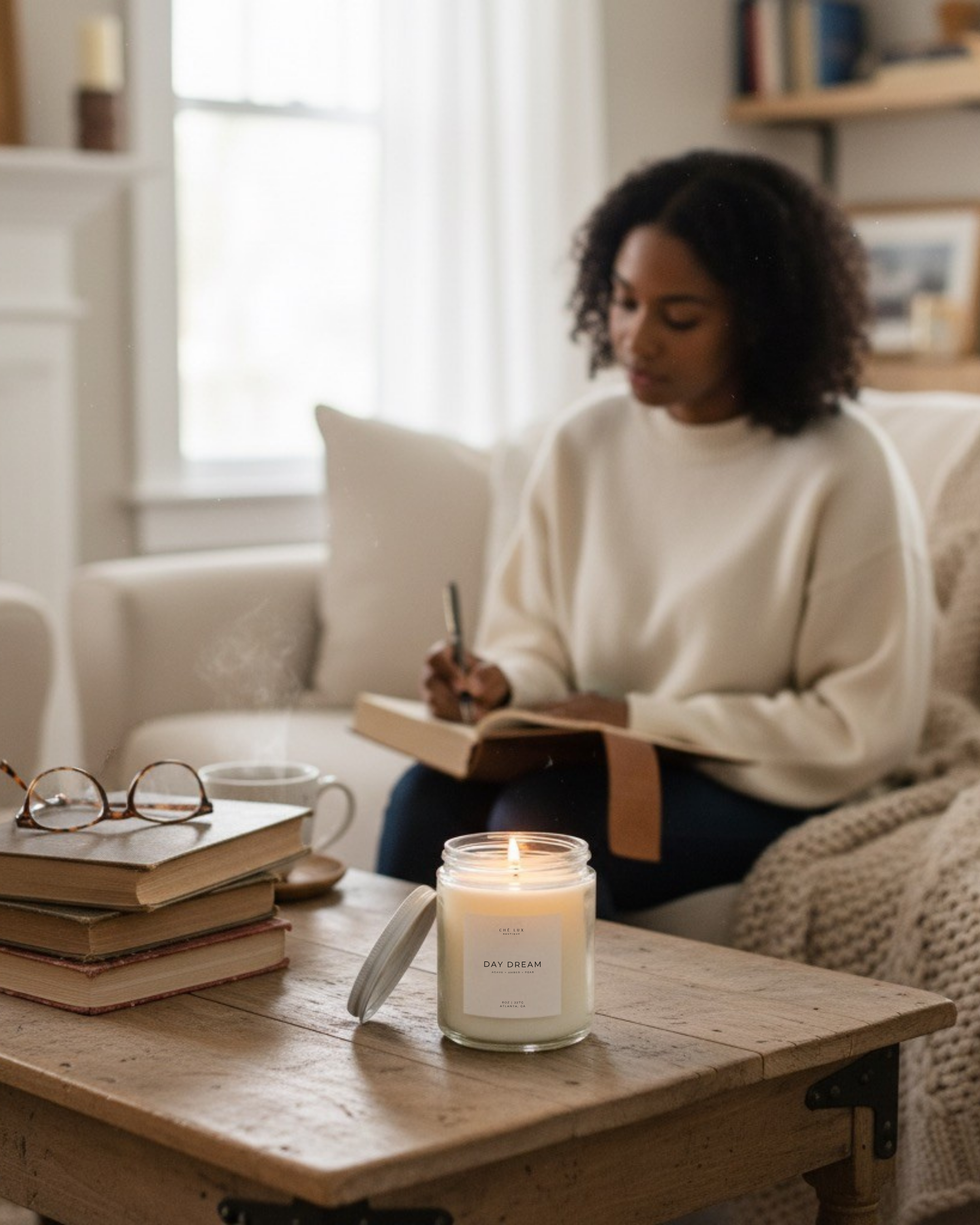 Woman sitting on a couch reading a book with a candle on a table in front of her.