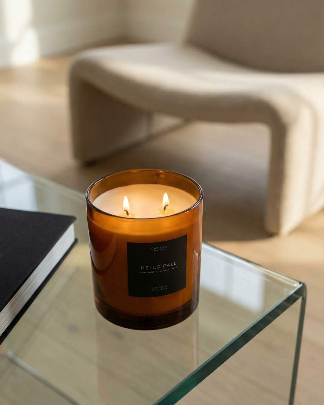 Candle in an amber glass jar on a glass table with a blurred chair in the background