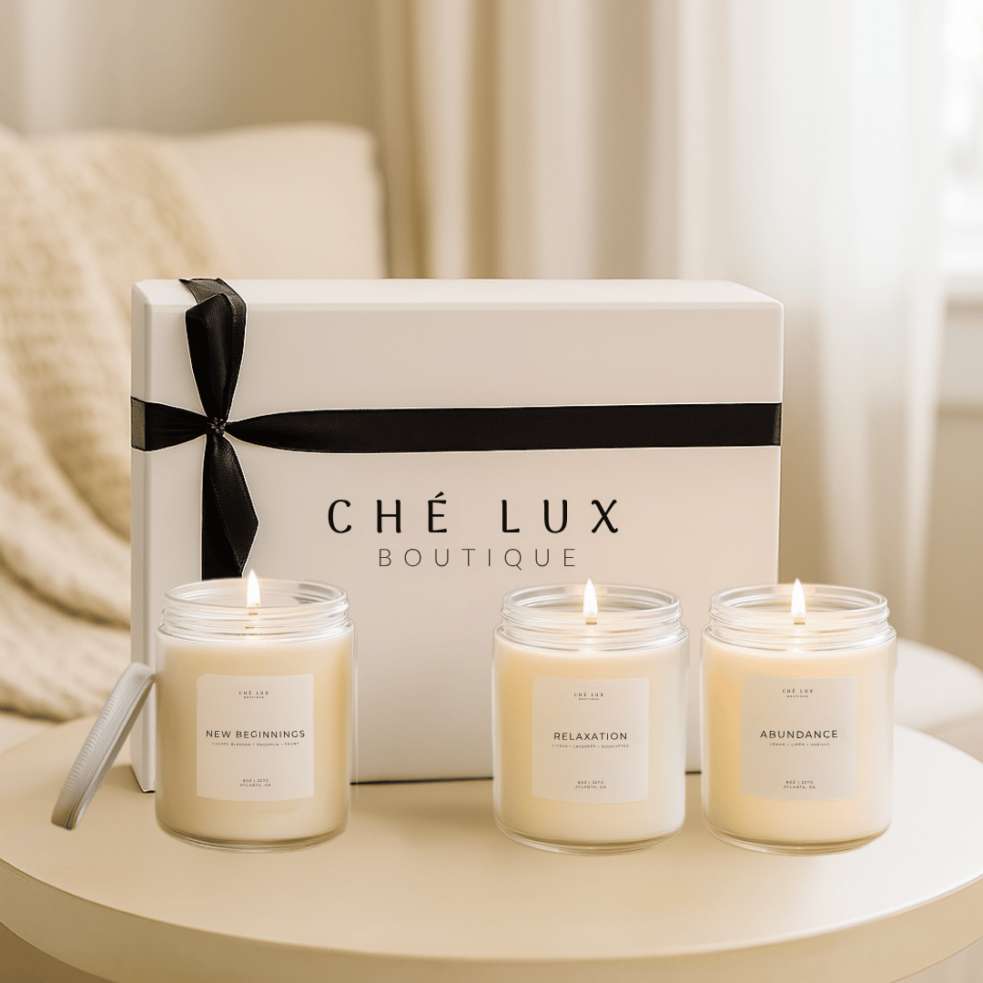 Three lit candles in front of a 'Che Lux Boutique' box on a table.