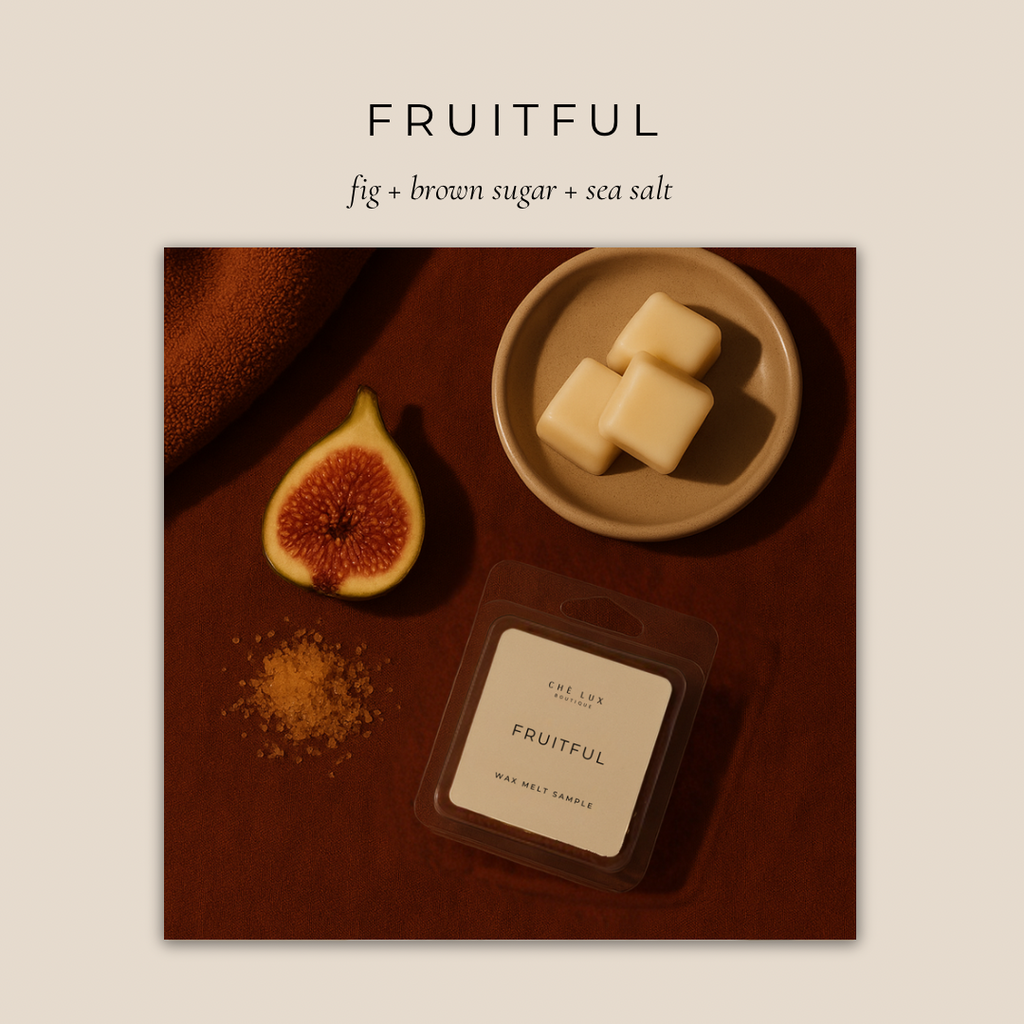 Product photography by CHE LUX BOUTIQUE displaying the Fruitful fig brown sugar sea salt wax melt sample, a cut fig with vibrant red flesh, a pile of golden brown sugar, and three creamy white wax melts on a small beige plate, all set on a warm reddish-brown surface